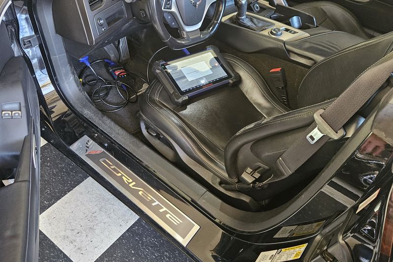 A Corvette with the door open and key programming equipment on the seat, being worked on in a garage.