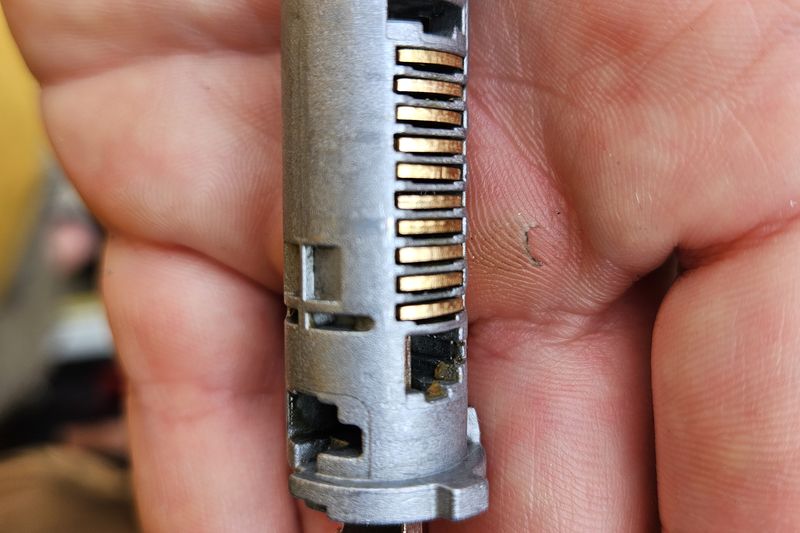 A worn lock cylinder removed from its housing, held in the palm of a hand.