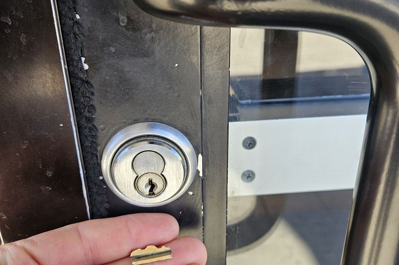 A key being fitted to the cylinder of a glass storefront door with a metal pull handle.